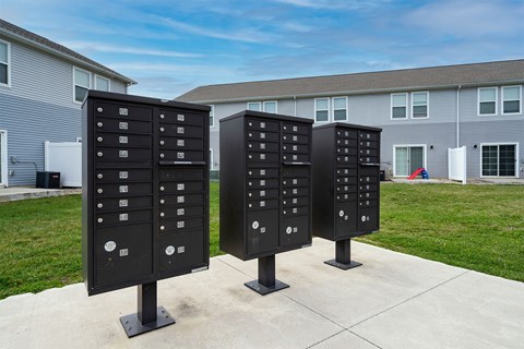 Three black mailboxes are standing on a sidewalk in front of a building.