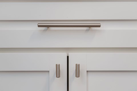 A white cabinet with a silver handle and a silver bar on top.