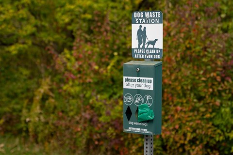 A sign for a dog waste station is displayed on a post.