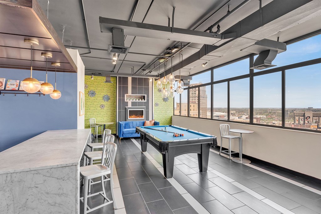 A pool table is in the middle of a room with a bar and a view of the city.