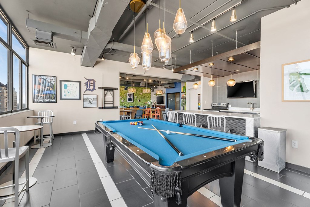 A pool table is in the middle of a room with a bar and a TV.