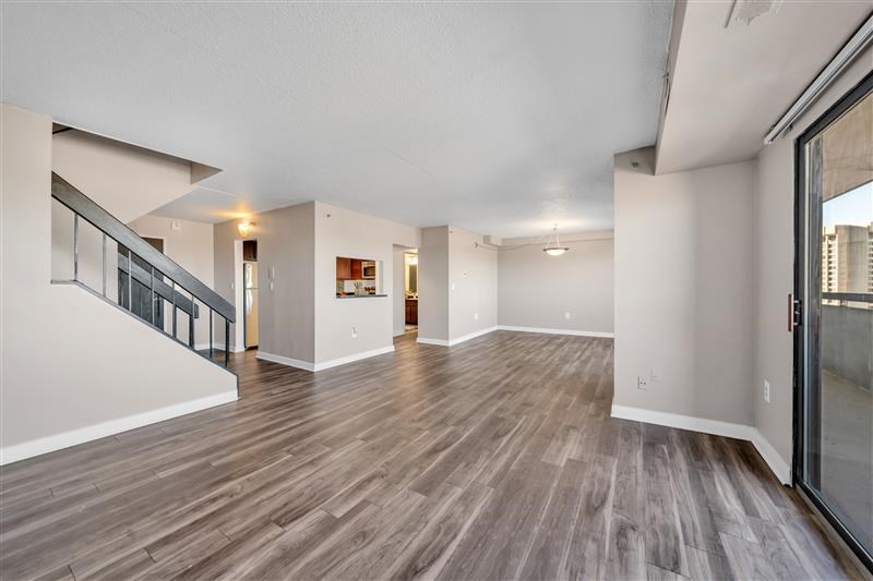 A spacious room with wooden flooring and a staircase on the left side.