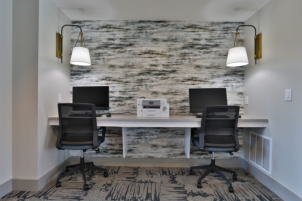 Two black chairs are positioned in front of a white desk with a laptop and monitor on it.