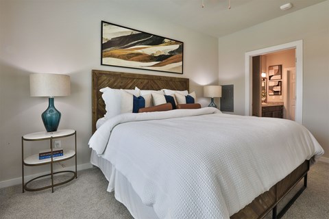 A bedroom with a large bed, a nightstand with a lamp, and a painting on the wall.