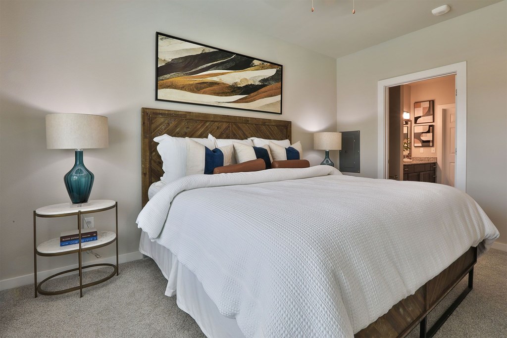 A bedroom with a large bed, a nightstand with a lamp, and a painting on the wall.