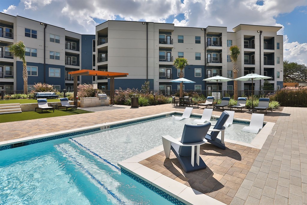 A swimming pool with a bench and umbrella in front of apartment buildings.