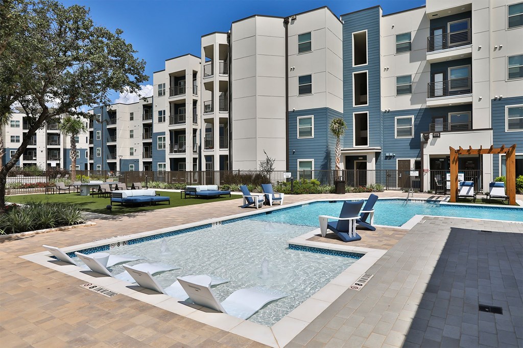 A swimming pool surrounded by lounge chairs and a building in the background.