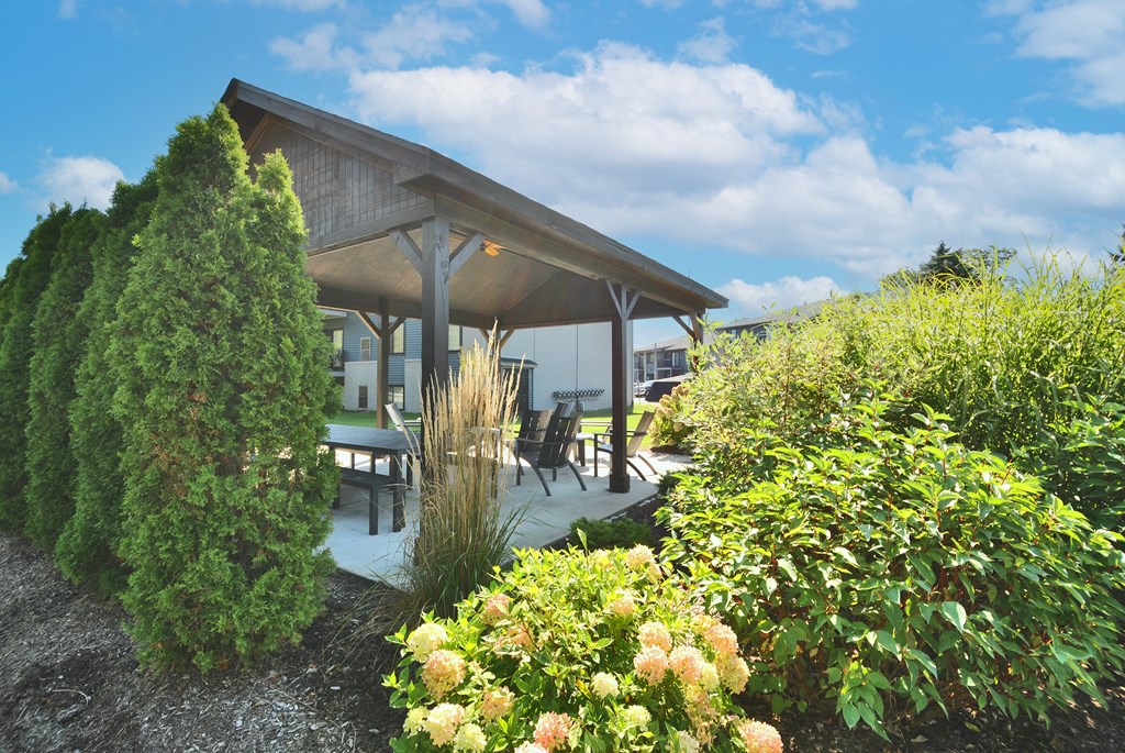 A wooden pavilion is surrounded by greenery and flowers.