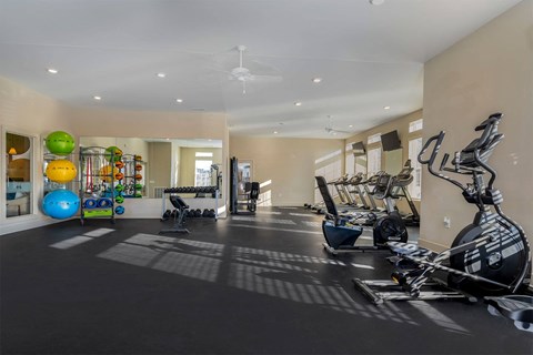 A gym with a variety of exercise equipment including treadmills, stationary bikes, and weights.