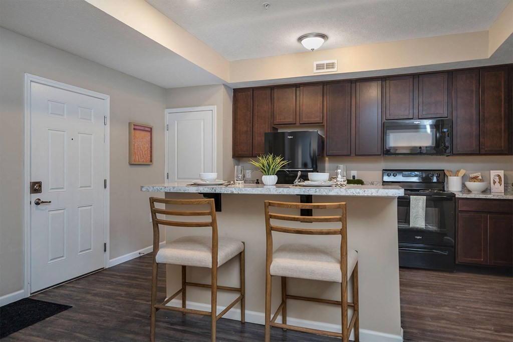 A kitchen with a black fridge, white cabinets, and a white island with two chairs.