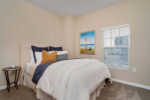 A bedroom with a bed, pillows, a nightstand, and a painting on the wall.