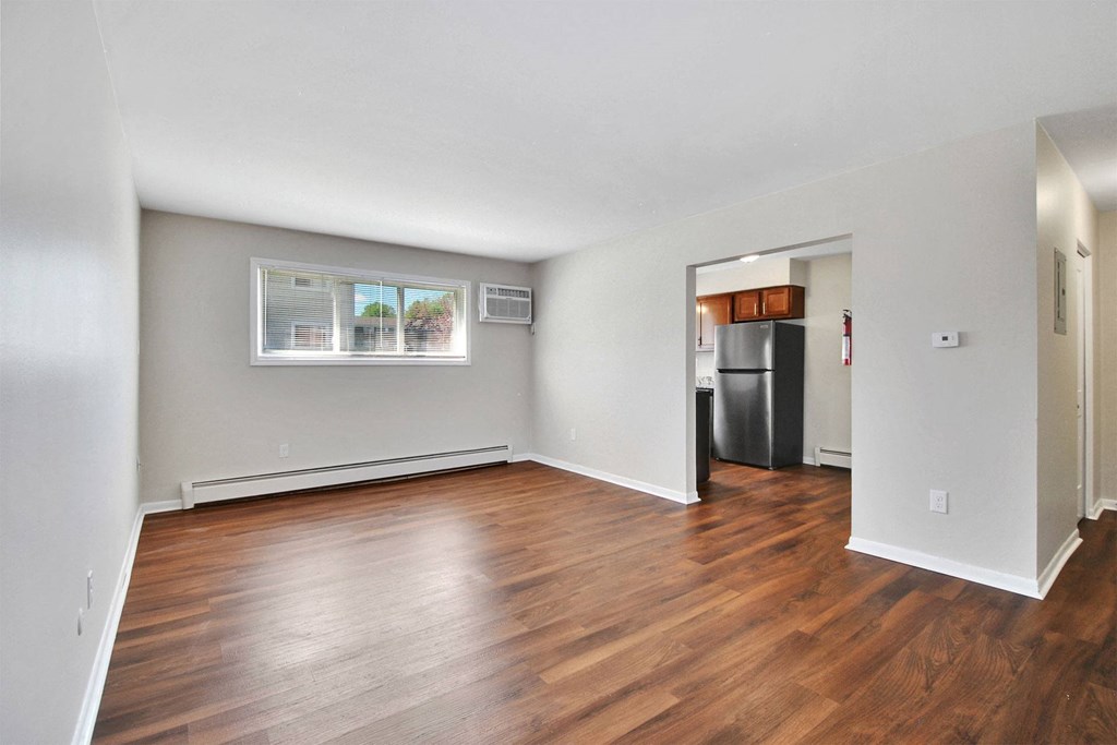 an empty living room with wood flooring and a kitchen