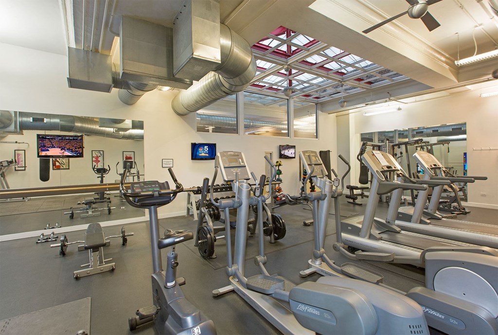 a gym with weights and cardio equipment and a tv