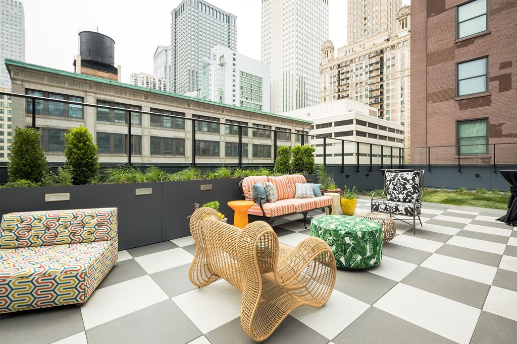 a rooftop lounge area with chairs and tables and skyscrapers
