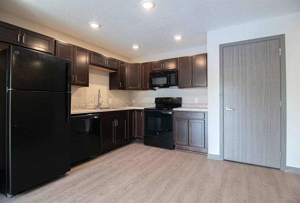 an empty kitchen with black appliances and dark wood cabinets