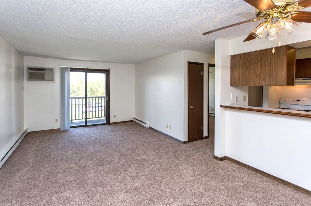 an empty living room with a ceiling fan and a door to a balcony