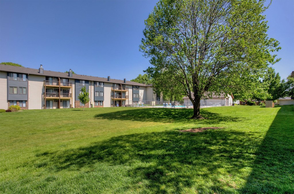a large lawn with a tree in front of an apartment building