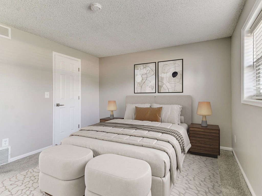 A bedroom with a large bed, two lamps, and two round ottomans.