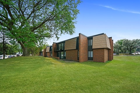 a row of brick apartments on a green lawn with a tree