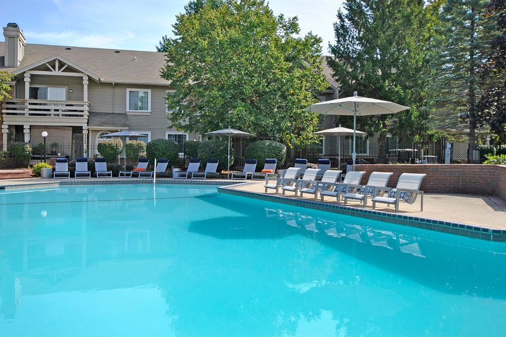 a swimming pool with chairs and umbrellas in front of a house