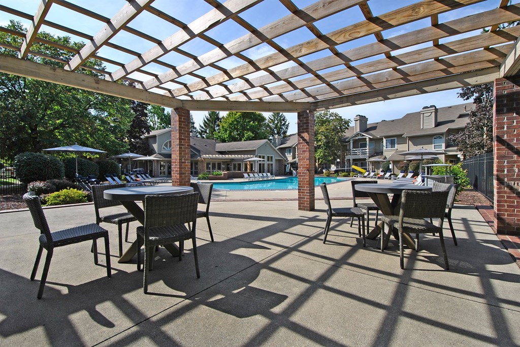 a covered patio with tables and chairs next to a swimming pool