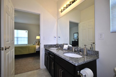 A bathroom with a sink, mirror, and a bed in the background.
