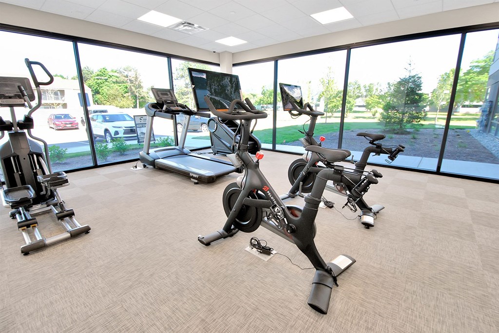 a gym with various exercise machines and a window view of a parking lot