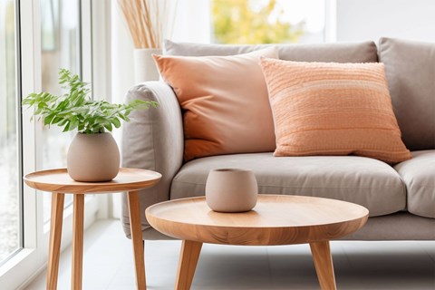 A living room with a grey couch, two round tables, and a potted plant.