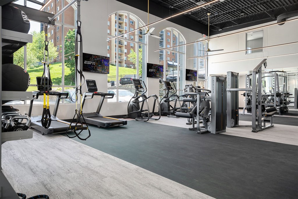 a gym with cardio machines and weights in a building with large windows