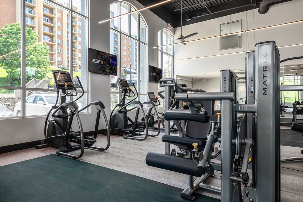 a gym with weights and cardio equipment in a building with large windows