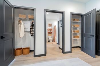 A hallway with a grey floor and a white rug, with three open doors on the left and right.