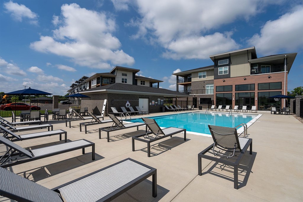 A pool area with sun loungers and a building in the background.