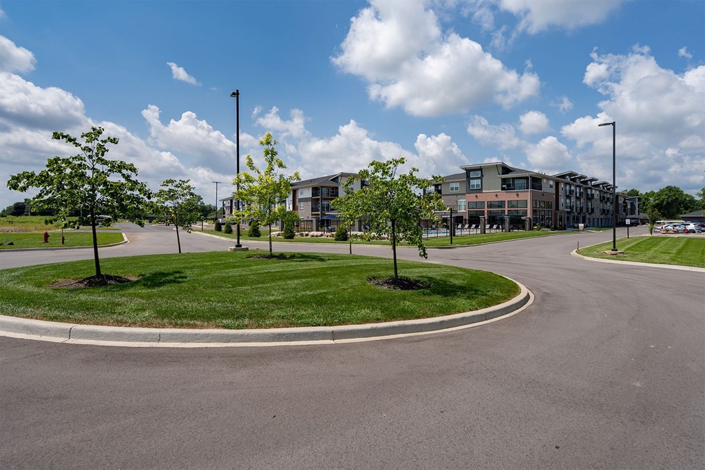 A roundabout with a grassy island in the middle and apartment buildings in the background.