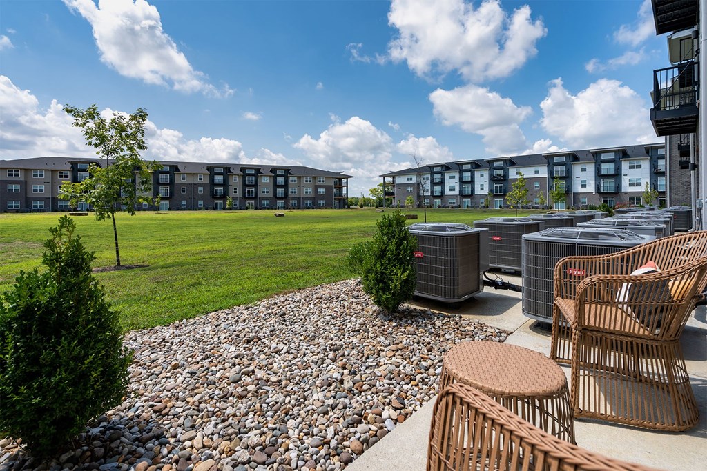 A patio area with chairs and a tree in front of apartment buildings.