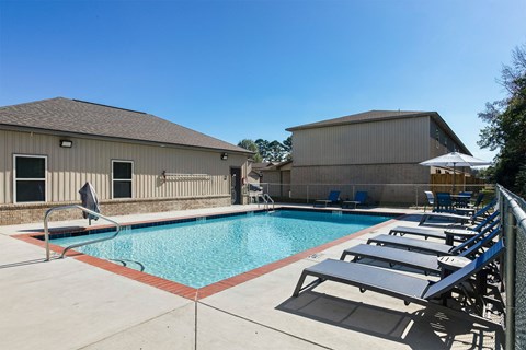 A pool with sun loungers and a building in the background.