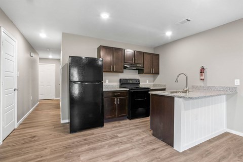 A kitchen with a black fridge, brown cabinets, and a white counter.