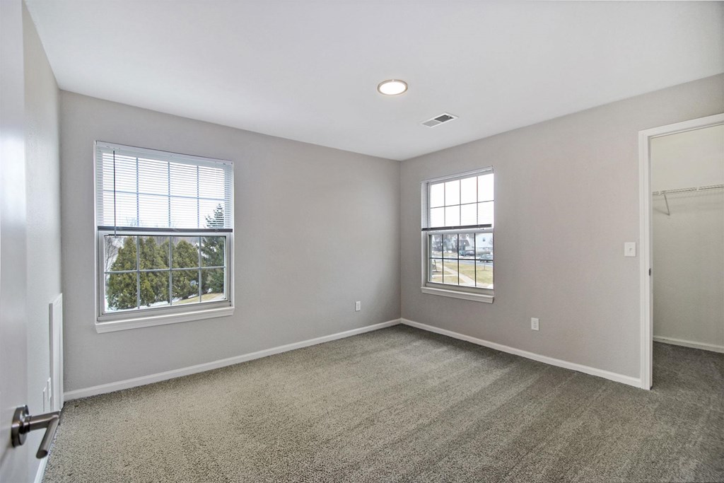 A spacious room with two windows and carpeted floor.