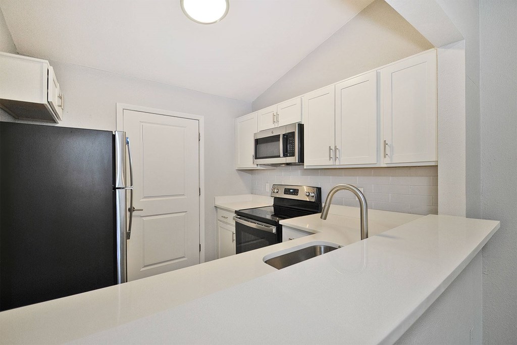 A black refrigerator sits next to a white sink in a kitchen.