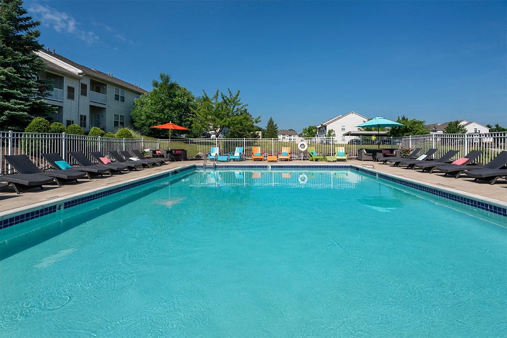 A swimming pool with a blue tinted water and sun loungers.