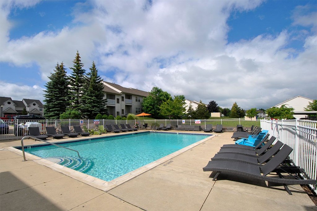 A pool surrounded by chairs and trees.