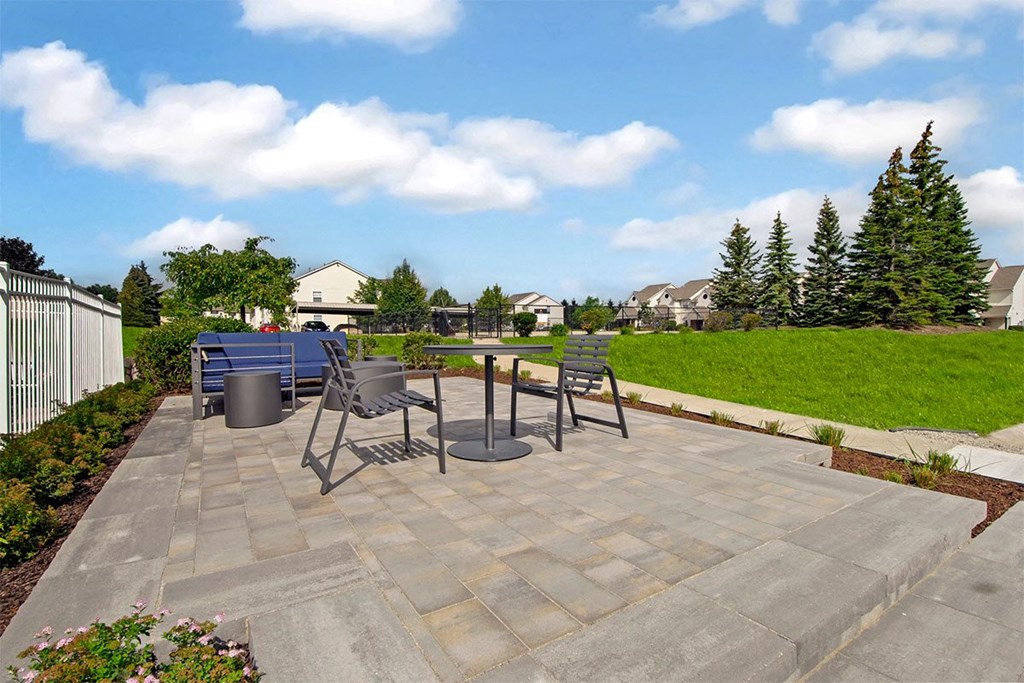 A patio with a table and chairs is surrounded by a green lawn.