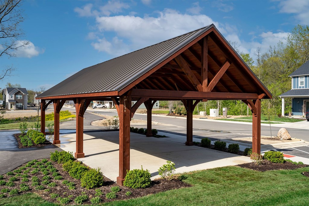 A pavilion with a brown roof and wooden pillars is surrounded by greenery.