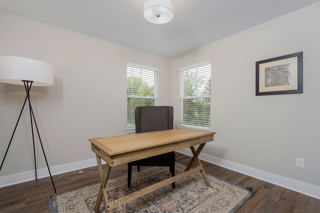 a room with a desk and a chair and two windows