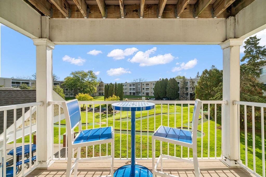 A white balcony with a table and chairs overlooking a green lawn.