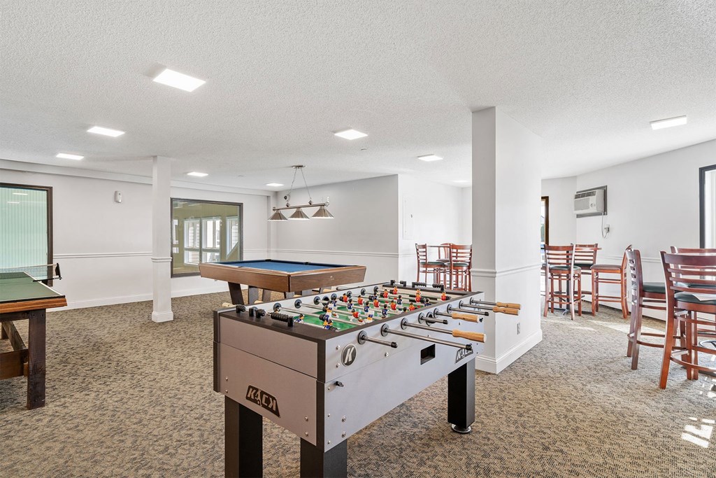 A foosball table is in the middle of a room with a pool table and chairs.