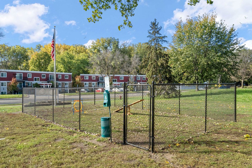 A green trash can sits in front of a chain link fence.