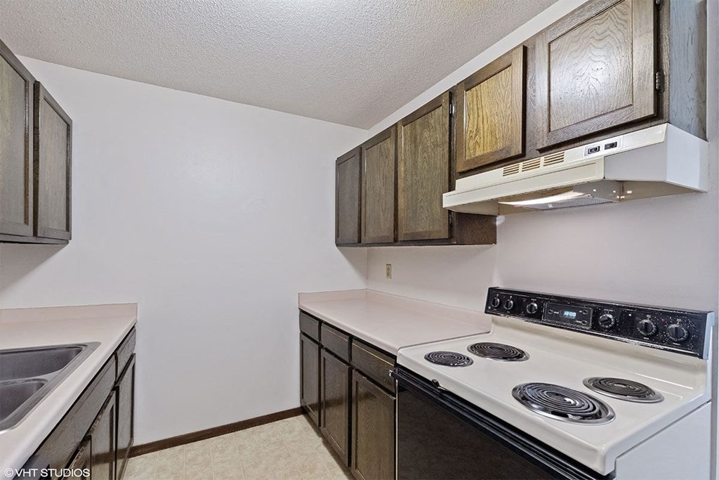 A kitchen with a white stove top oven and wooden cabinets.