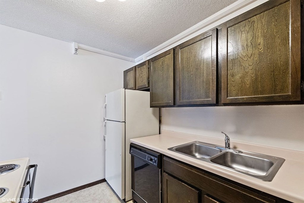 A kitchen with a white refrigerator, a stainless steel sink, and wooden cabinets.