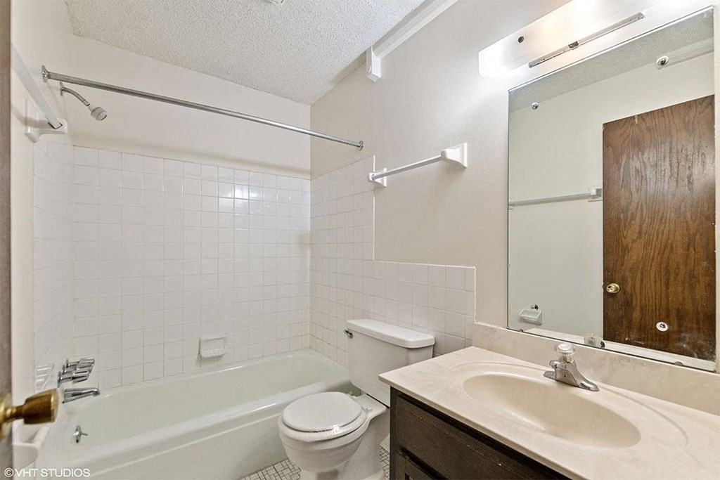 A white tiled bathroom with a toilet, sink, and bathtub.