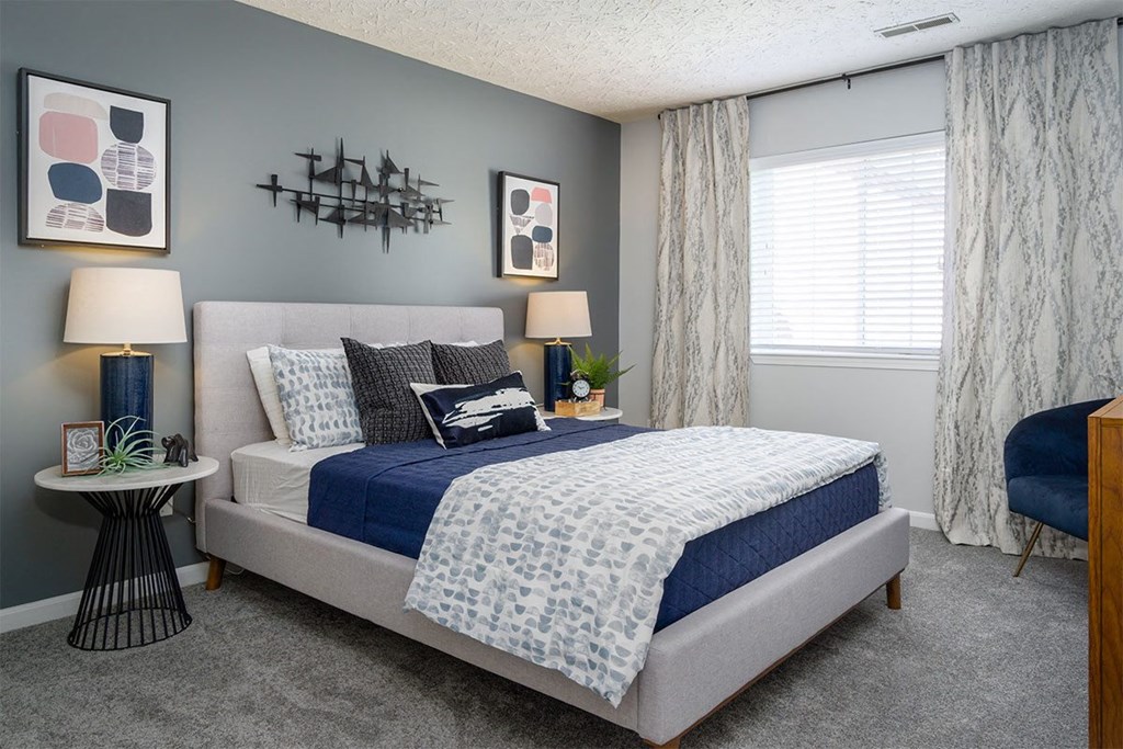 A bedroom with a bed, two lamps, a nightstand, and a chair.